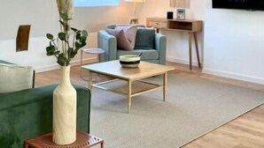 En moderne stue med en grøn sofa, et træbord og et lille sofabord. Et vindue med udsigt til himlen, og et maleri på væggen.