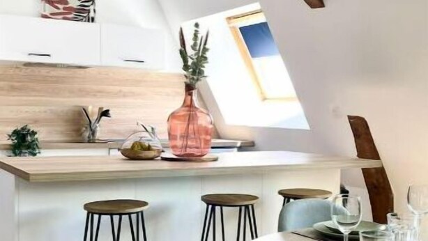 Et moderne køkken med træloft, ovenlys og et spiseområde med barstole samt et bord dækket til to.
