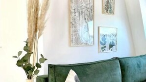 En grøn sofa med en dekorativ pude, en vase med pampas og to billeder på væggen.