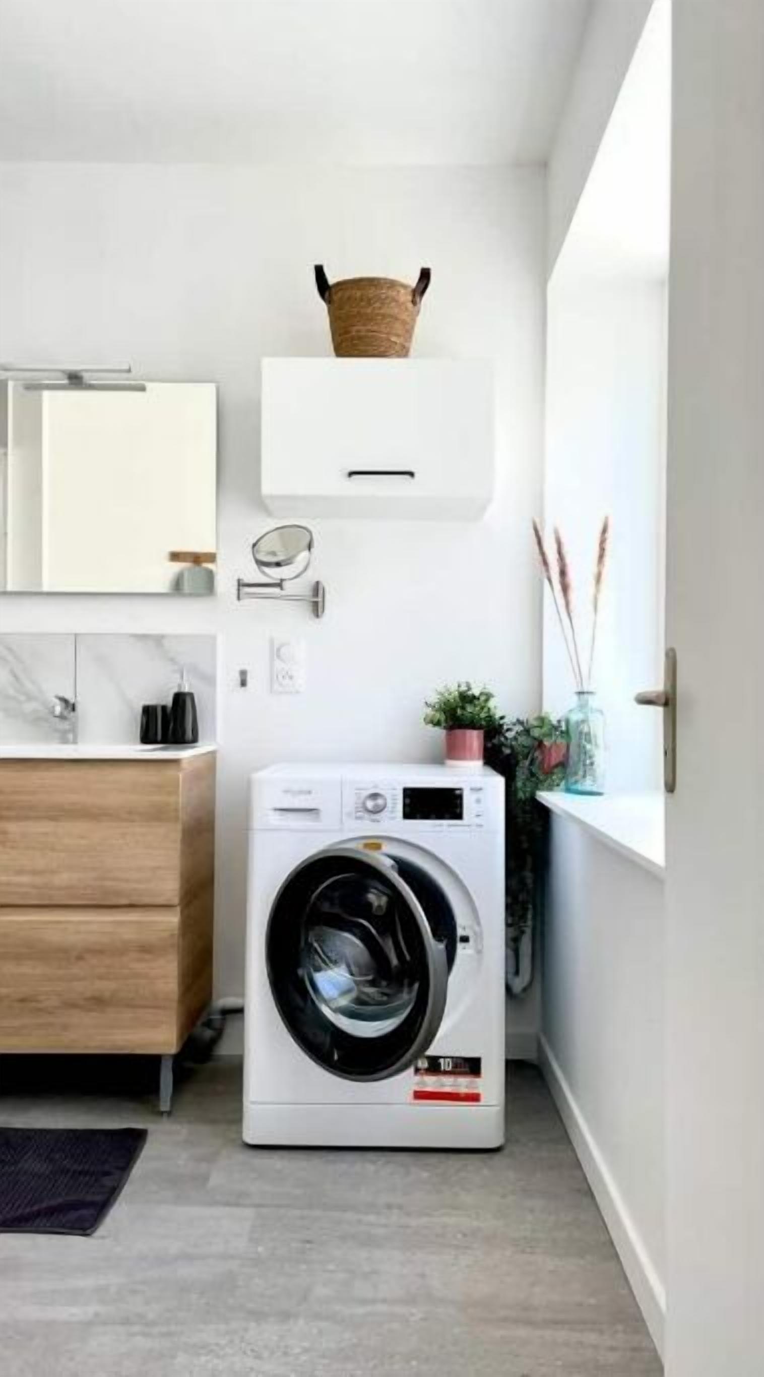 Un espace buanderie compact comprenant un lave-linge à chargement frontal, un meuble en bois et une petite étagère avec des objets décoratifs.