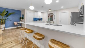 Eine moderne Küche mit weißer Arbeitsplatte, Barhocker, einem Edelstahlkühlschrank und einer blauen Akzentwand.