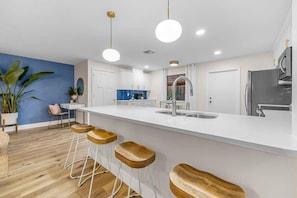 A modern kitchen with white cabinets, a stainless steel refrigerator, and a large island with bar stools.