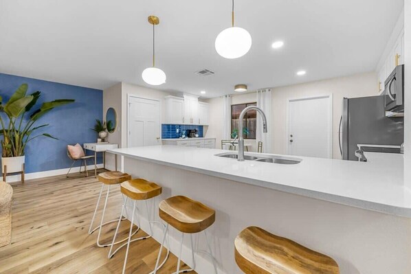 A modern kitchen with white cabinets, a stainless steel refrigerator, and a large island with bar stools.