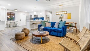 Ein modernes Wohnzimmer mit einem blauen Sofa, Korbstühlen, einem Couchtisch und einem Deckenventilator.