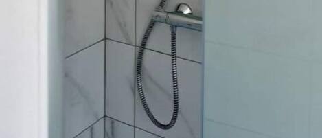 A shower with a handheld showerhead and a flexible hose, set against a tiled wall with a marble pattern.