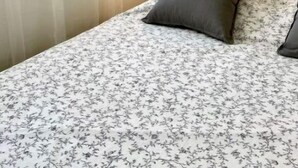 Une chambre à coucher comprenant un lit, une lampe de chevet, une fenêtre avec des rideaux légers et une étagère murale agrémentée d’objets décoratifs.