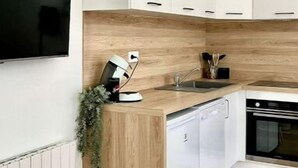 Une cuisine moderne avec des armoires blanches, un plan de travail en bois, un lave-vaisselle encastré et un téléviseur fixé au mur.