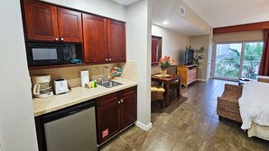 A modern kitchen with wooden cabinets, a built-in microwave, and a dishwasher. There is a dining area with a table and chairs, and a balcony with a view of palm trees. - Luau Two 6426 Studio, balcony, tram, wifi. Awesome Views! (Miramar Beach)