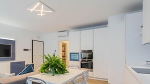 Eine moderne Küche mit integrierten Geräten, eine Essecke mit großem Tisch und ein an der Wand befestigter Fernseher.