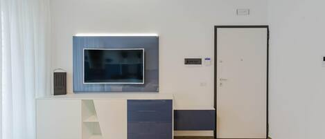 Een moderne kamer met een wit en blauw bureau, een flatscreen televisie, een deur en een kleine plant.