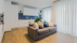 Ein modernes Wohnzimmer mit einem braunen Sofa, einem Esstisch und einer Küche im Hintergrund.