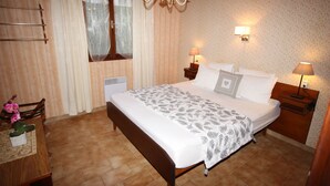 A bedroom with a bed, two bedside tables with lamps, a chandelier, a window with curtains, and a wooden chair. - Villa Altea 2 Dans un Splendide Parc Fleuri, Calme à 900 Mètres de la Plage (Calvi)