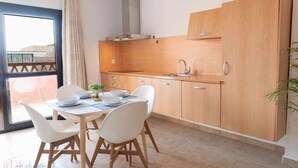 A modern kitchen with wooden cabinets, a sink, and a dining area with white chairs and a table.