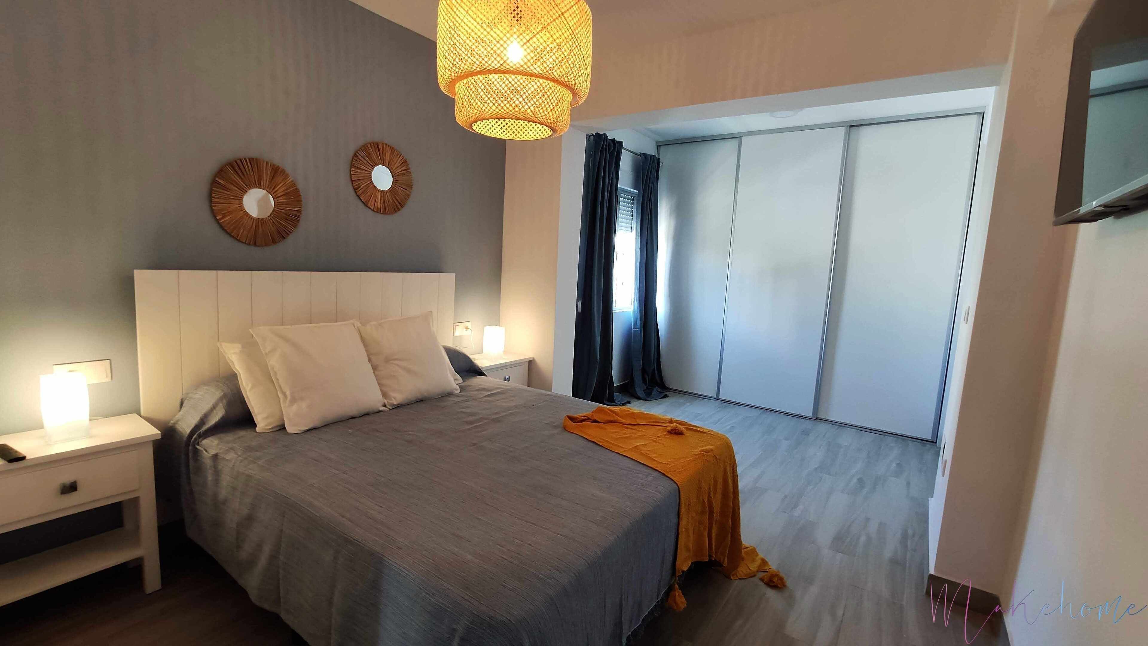 Un dormitorio con cama, mesitas de noche, lámpara colgante y vistas a un puertas correderas.