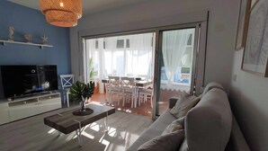 A modern living room with a flat-screen TV, a wooden coffee table, and a sofa. There is a dining area with a table and chairs visible through a glass door. - En la Misma Playa Nuevo 3 Dormit , Vistas al mar (Punta Umbria)