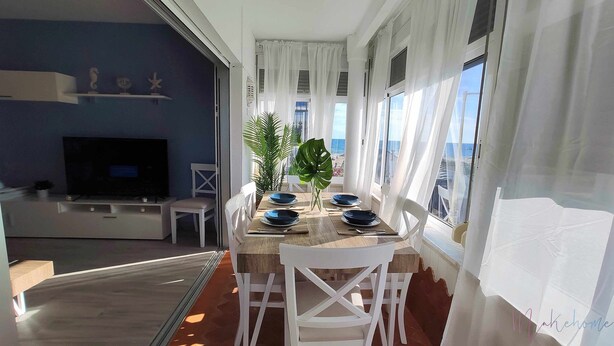 A dining area with a table set for four, a television in the background, and a view of the sea through large windows. - En la Misma Playa Nuevo 3 Dormit , Vistas al mar (Punta Umbria)