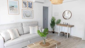 A modern living room with a light grey sofa, a wooden coffee table, and a small side table with candles. There are framed artworks on the wall and a potted plant. - En la Misma Playa Nuevo 3 Dormit , Vistas al mar (Punta Umbria)