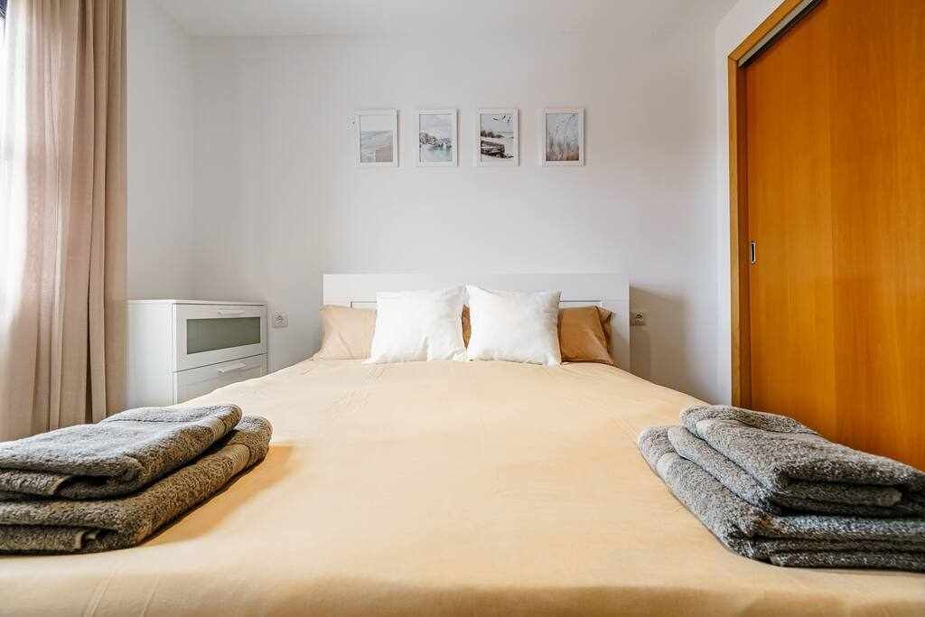 Una habitación de hotel con cama, almohadas, una puerta de madera y una mesita de noche pequeña.