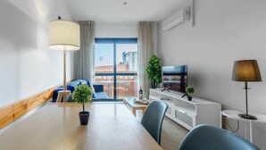 A modern living room with a wooden dining table, a sofa, a TV, and a plant.