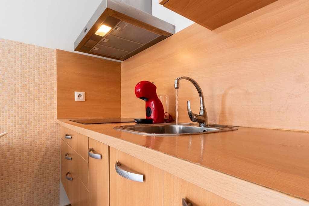 Eine Küche mit Spüle aus Edelstahl, Holzschränken und einem roten Wasserkocher.