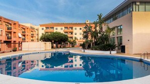 A swimming pool surrounded by multi-story buildings with balconies, reflecting the architecture.