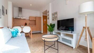 Een moderne woonkamer met een bank, een televisie, een kleine ronde tafel en een keuken op de achtergrond.