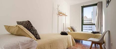 A hotel room with two beds, a chair, a coat rack, and a large window.