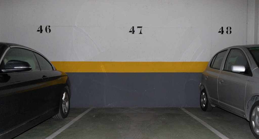 Un aparcamiento con dos coches estacionados en plazas adyacentes, identificadas con los números 46 y 47.