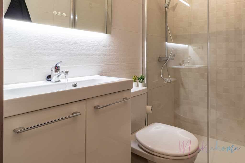 Une salle de bain moderne avec un lavabo blanc, des toilettes et une douche séparée par une paroi de verre.