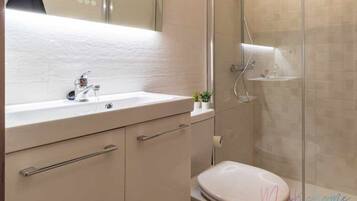 Une salle de bain moderne avec un lavabo blanc, des toilettes et une douche séparée par une paroi de verre.