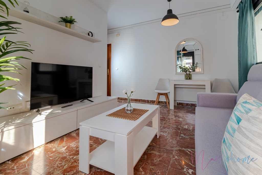 A modern living room with a flat-screen TV, white furniture, a coffee table, and a sofa.