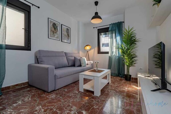 Un salon moderne avec un canapé gris, une table basse blanche, un lampadaire et une grande plante en pot.