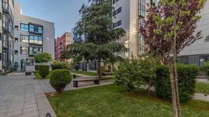 Ein moderner Innenhof in der Stadt mit einem gepflasterten Weg, ordentlich geschnittenen Büschen und einigen Bäumen.