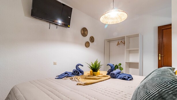 A bedroom with a bed, a television mounted on the wall, a hanging light fixture, and a wardrobe. - A Estrenar Pleno Centro, Parking (Huelva)