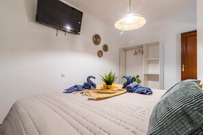 A bedroom with a bed, a television mounted on the wall, a hanging light fixture, and a wardrobe.