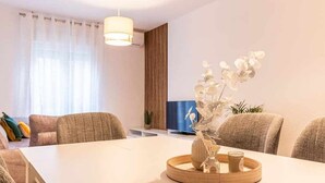 A modern hotel room with a dining table, chairs, a vase with flowers, and a television. - A Estrenar Pleno Centro, Parking (Huelva)