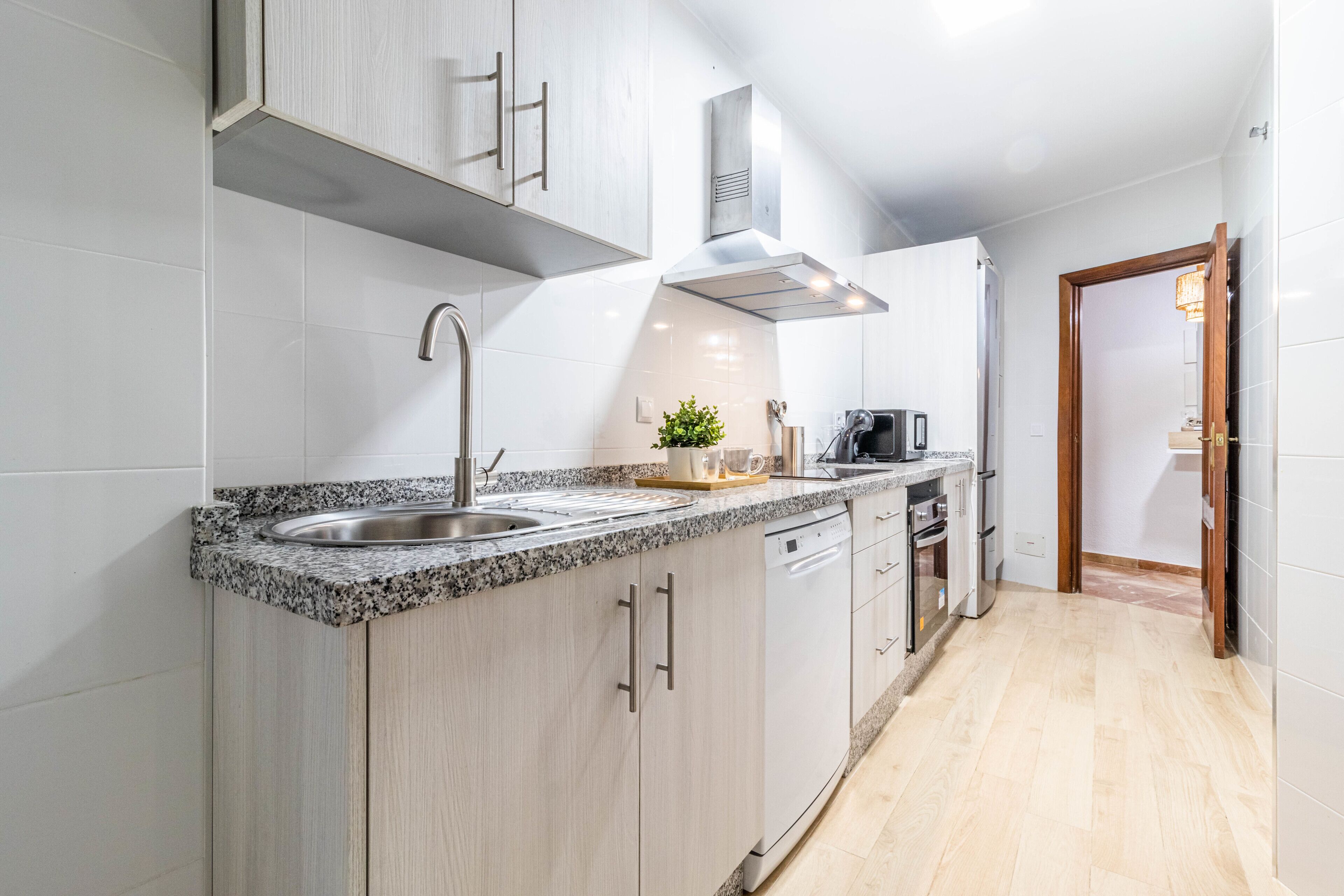 Een moderne keuken met granieten aanrechtbladen, roestvrijstalen apparatuur en kastjes van licht hout.