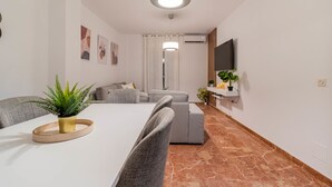 A modern living room with a dining area, grey sofas, a flat-screen TV, and a potted plant. - A Estrenar Pleno Centro, Parking (Huelva)