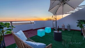 A rooftop terrace with a view of the sunset, a large umbrella, and seating areas. - Chalet en la Misma Playa (Punta Umbria)