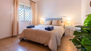 A hotel room with a large bed, two bedside tables, a window with curtains, and a potted plant. - Chalet en la Misma Playa (Punta Umbria)