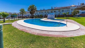 A swimming pool with a curved design, surrounded by a paved area and grass.