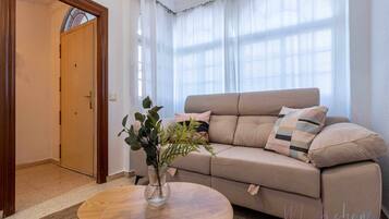A living room with a beige sofa, a round wooden coffee table, and a potted plant.