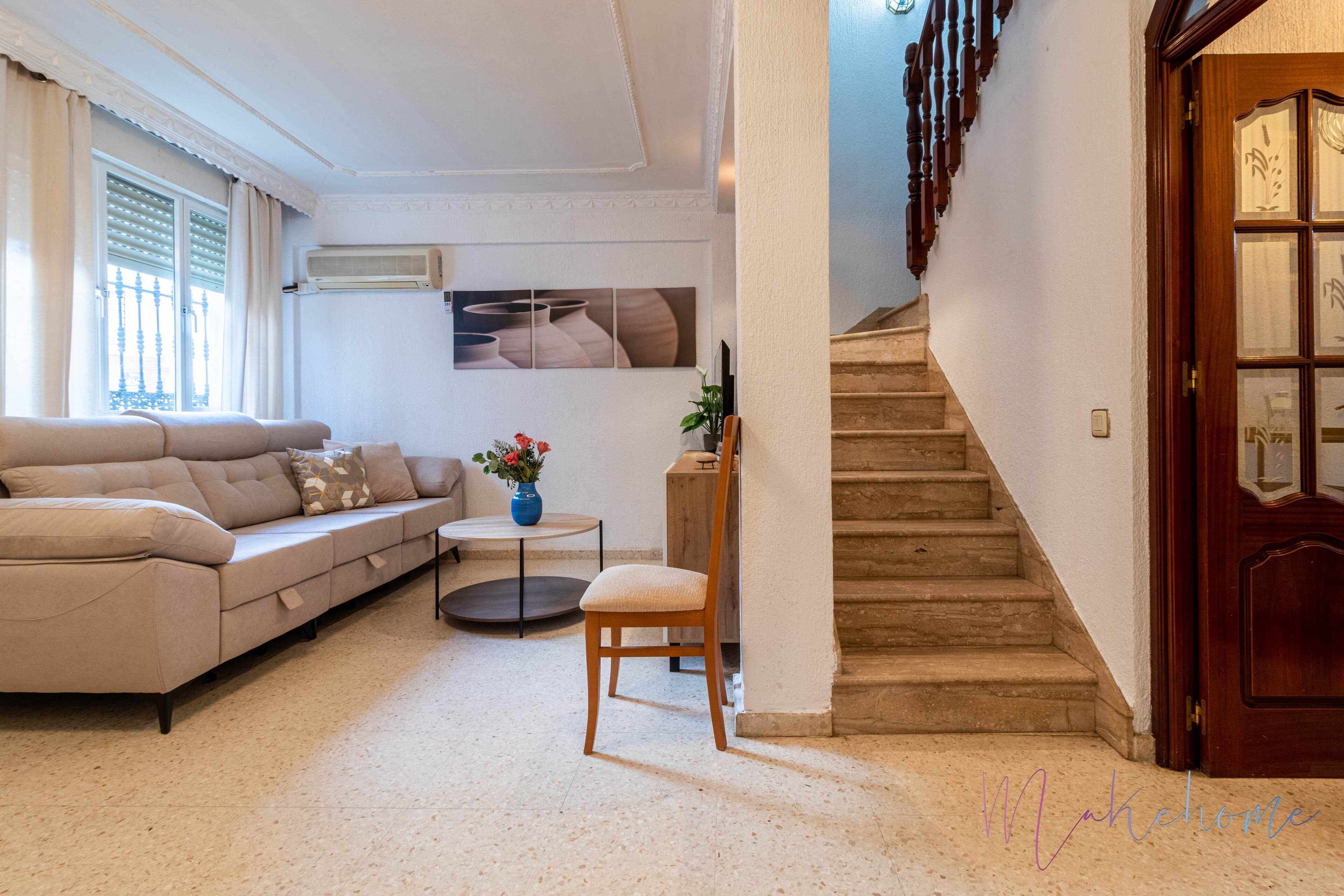 A living room with a sofa, a chair, a small table, and a staircase.