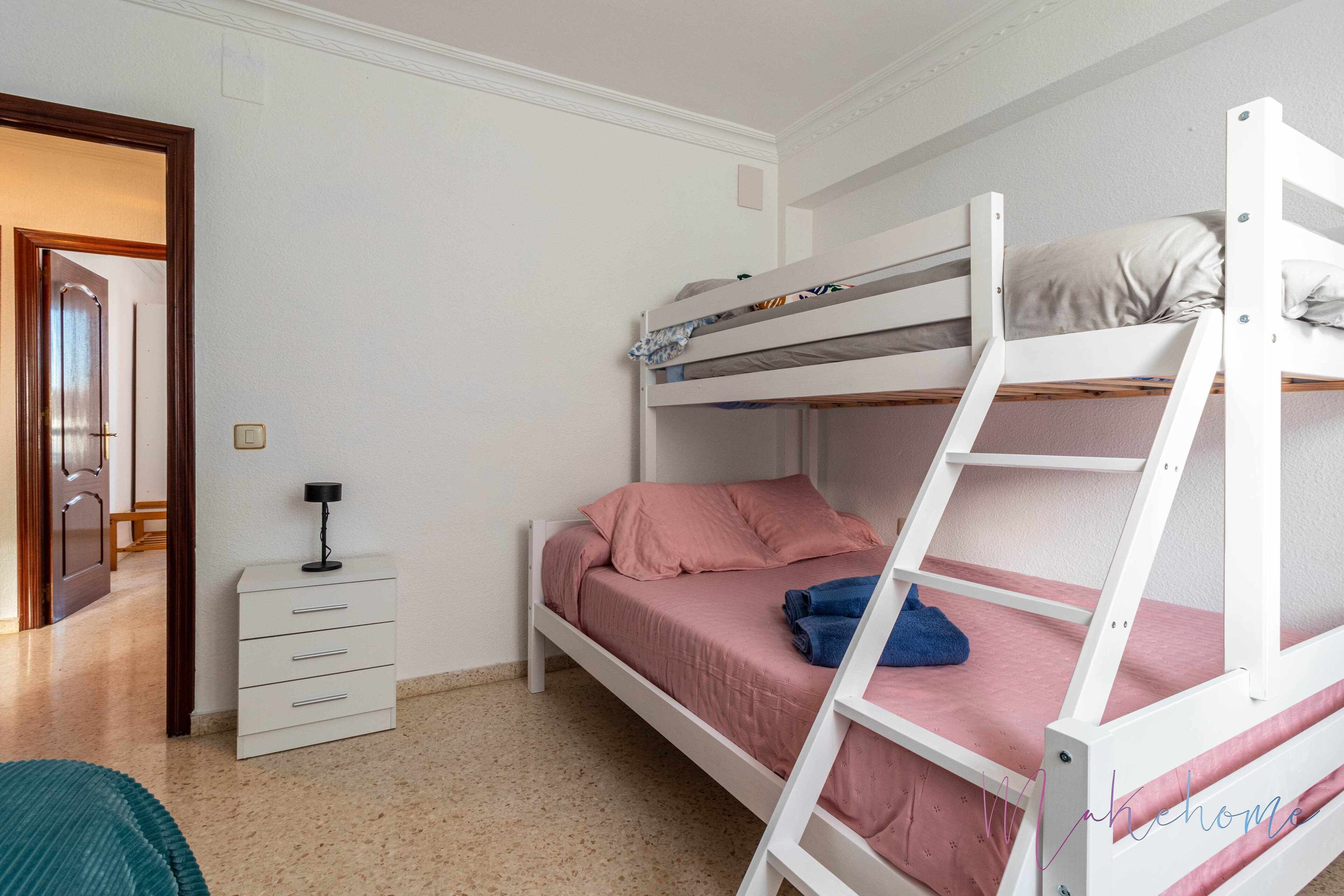 Quarto com beliche, cômoda branca e porta que dá para outro espaço.