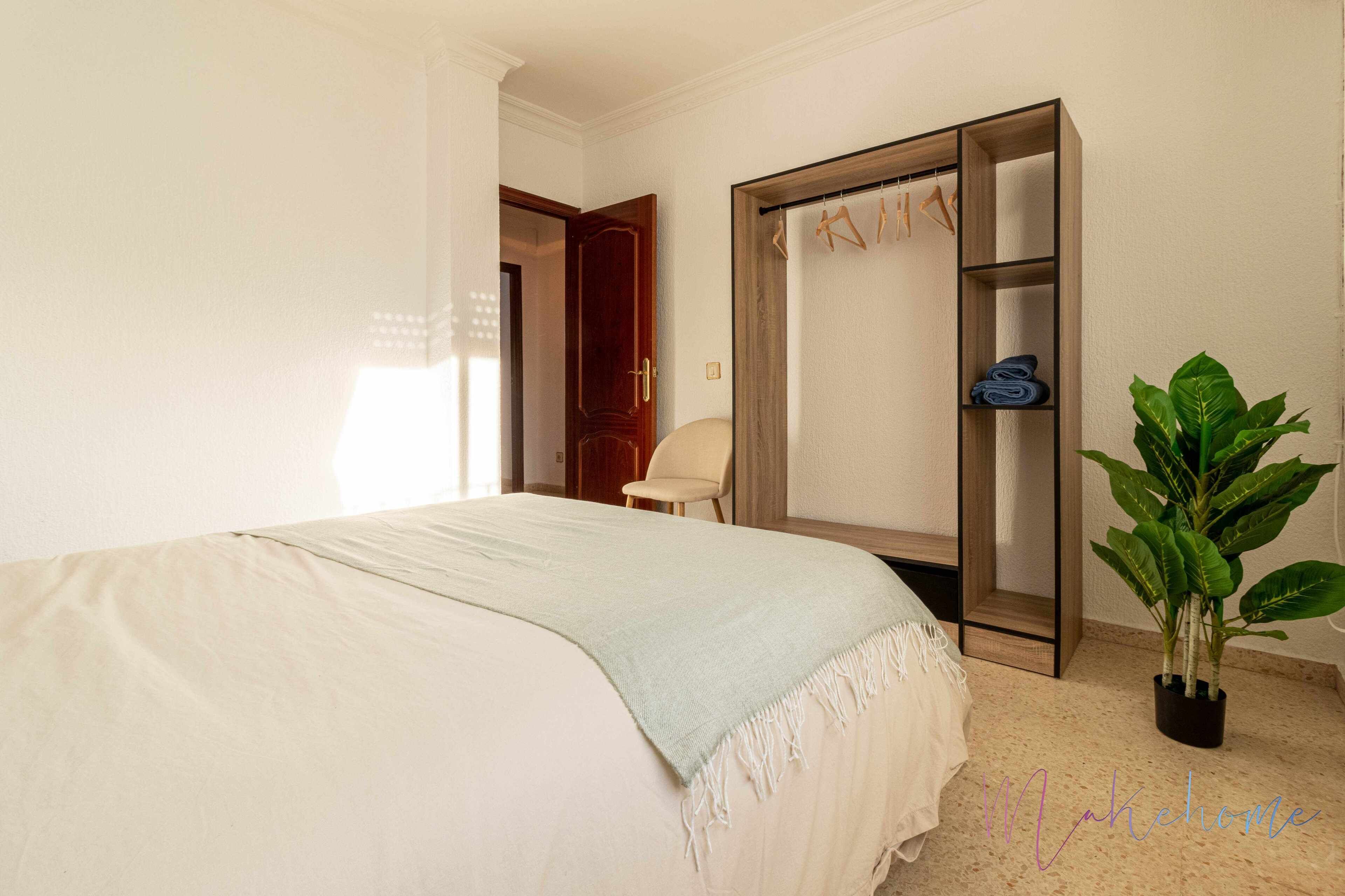 A bedroom with a bed, a wardrobe, a chair, and a potted plant.