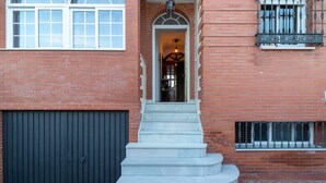 A brick building with a black garage door, a set of stone steps leading to an entrance, and a small balcony with a metal railing.