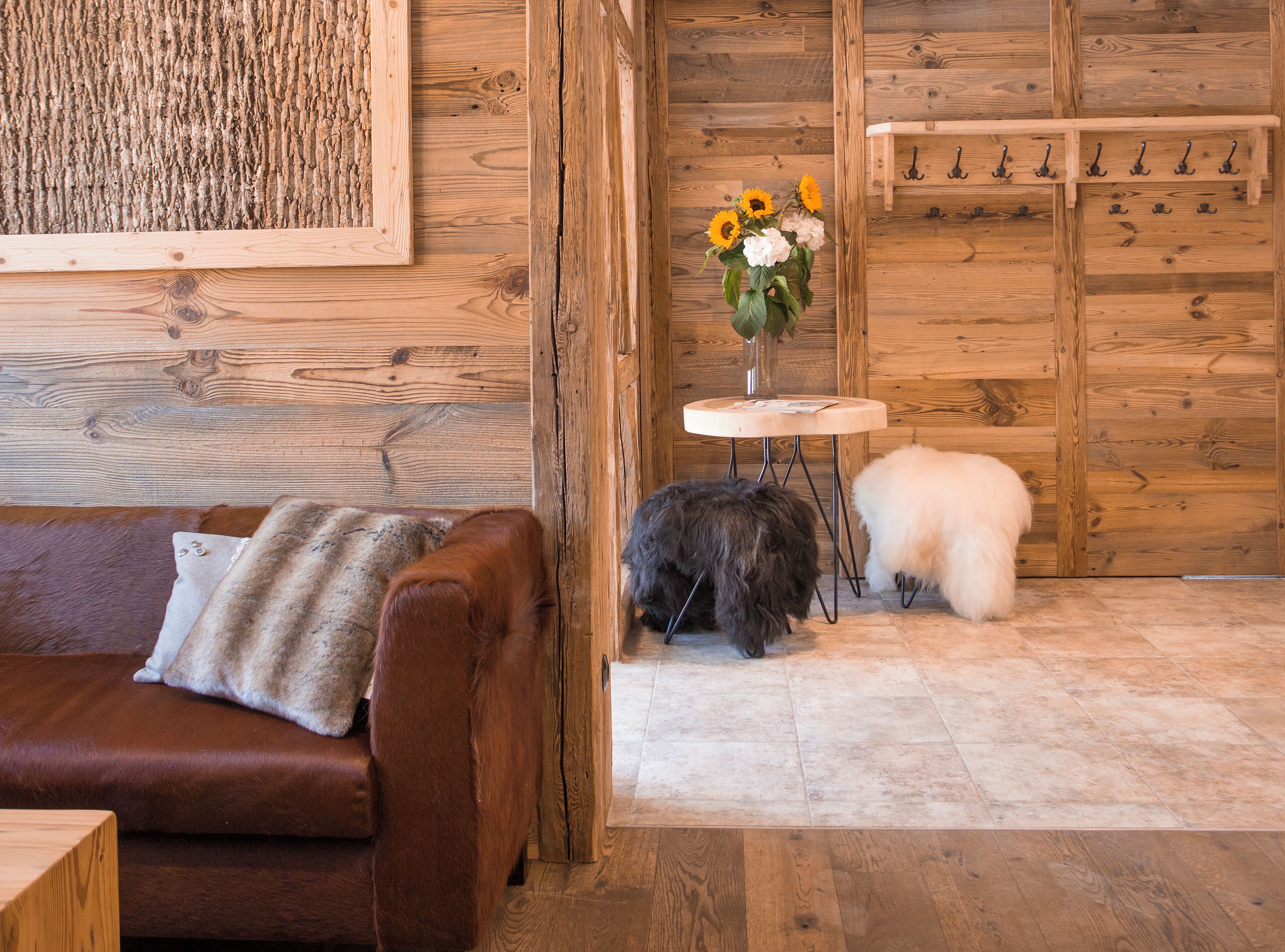 A wooden interior with a brown leather couch, a small round table with a vase of flowers, and a white fluffy dog.