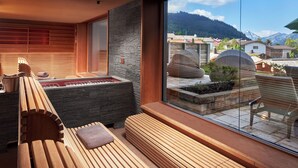 A modern spa area with wooden benches, a stone wall, and a view of a mountainous landscape. - Alpin Chalets Oberjoch (Bad Hindelang)