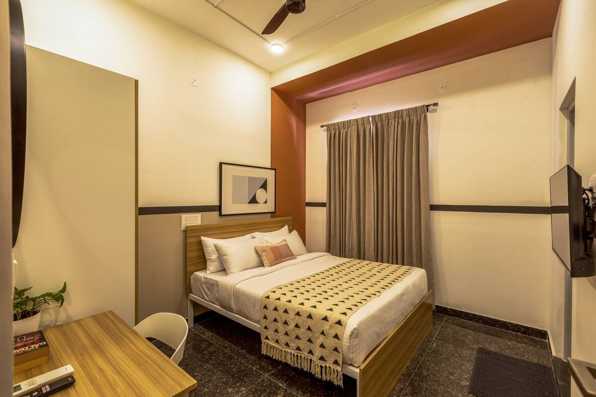 A hotel room with a bed, a desk, a chair, a television, and a window with curtains.