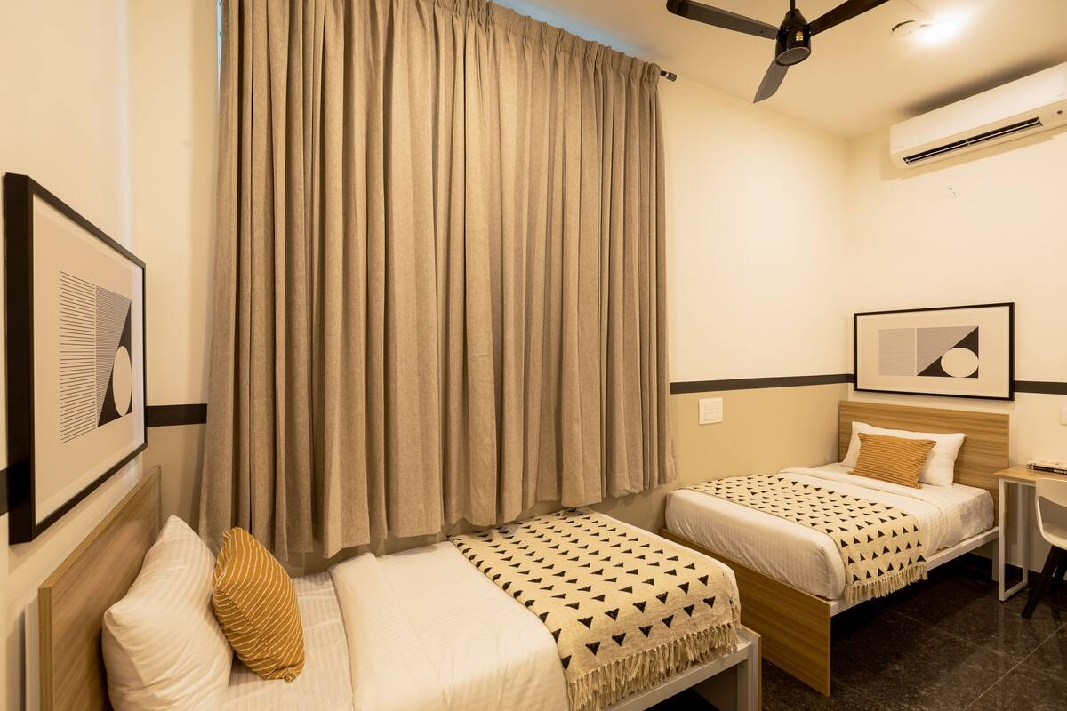 A hotel room with two beds, a ceiling fan, an air conditioning unit, and framed artwork on the walls.